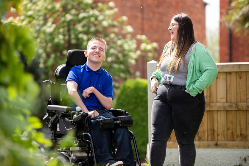 A resident using a powered wheelchair chatting with staff in the garden at Westholme