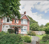 Red-brick exterior of Bryn Irfon with bay windows, a tiled gable and a front garden with shrubs and a path