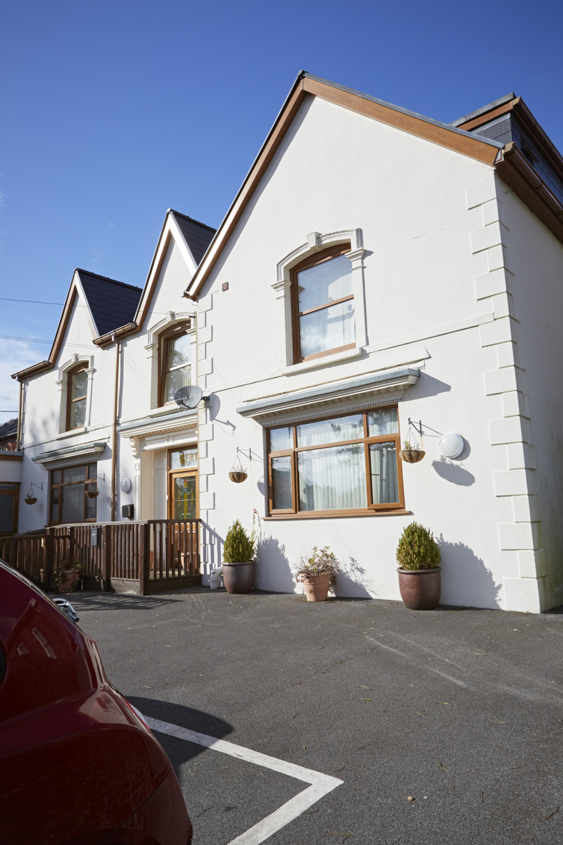 Front exterior of Isfryn, a white rendered house with gabled roofs, a ramped entrance and potted plants