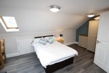 Loft bedroom at Willow Lodge with a double bed, teal accent wall, skylight and cream wardrobe and drawers