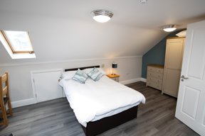 Loft bedroom at Willow Lodge with a double bed, teal accent wall, skylight and cream wardrobe and drawers