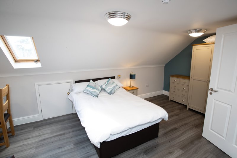 Loft bedroom at Willow Lodge with a double bed, teal accent wall, skylight and cream wardrobe and drawers