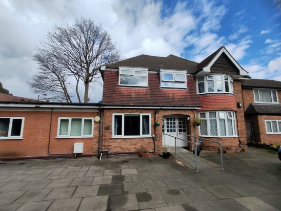 Front exterior of Evergreen, a red-brick care home with the name sign above the entrance and a paved forecourt