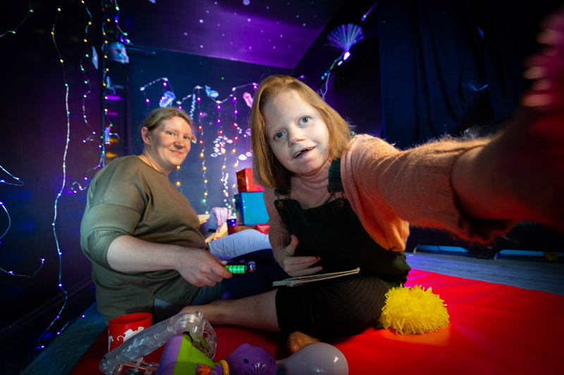 Resident and support worker relaxing among fairy lights and sensory toys in the sensory room at The Haven