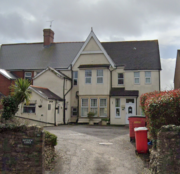 Exterior view of Bayview Lodge, a cream-rendered detached care home with a gabled roof and gravel driveway