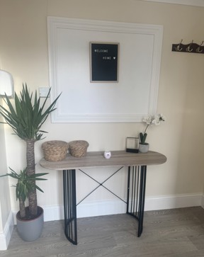 Hallway at Ty Camlas with a console table, a Welcome Home letterboard sign, a tall yucca plant and wall coat hooks