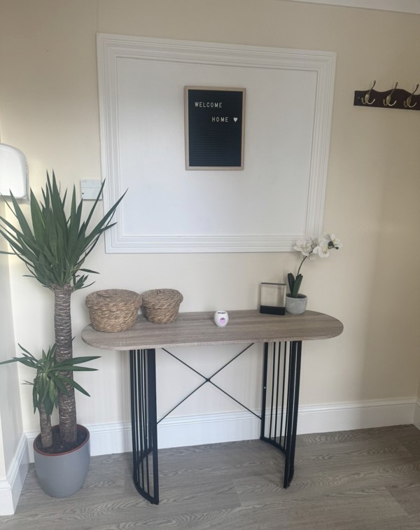 Hallway at Ty Camlas with a console table, a Welcome Home letterboard sign, a tall yucca plant and wall coat hooks