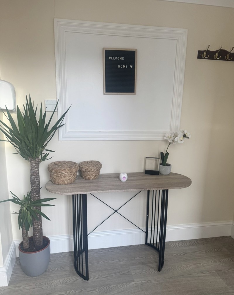 Hallway at Ty Camlas with a console table, a Welcome Home letterboard sign, a tall yucca plant and wall coat hooks