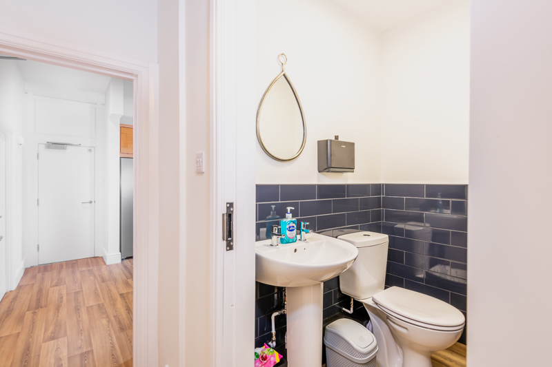 Cloakroom at Brynawel with a pedestal basin, dark blue metro tiles and a teardrop mirror
