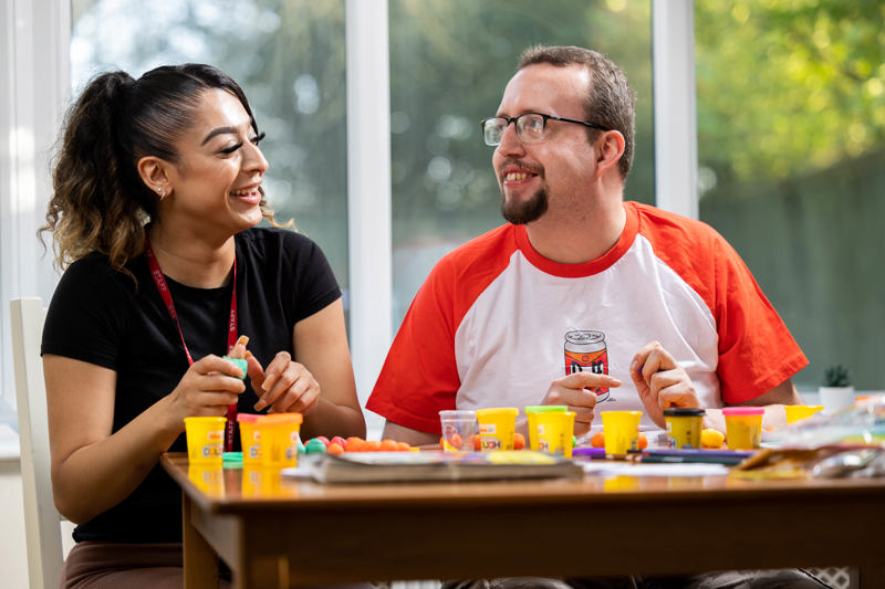 A support worker and a resident making models with play dough at a table at Cae Deri