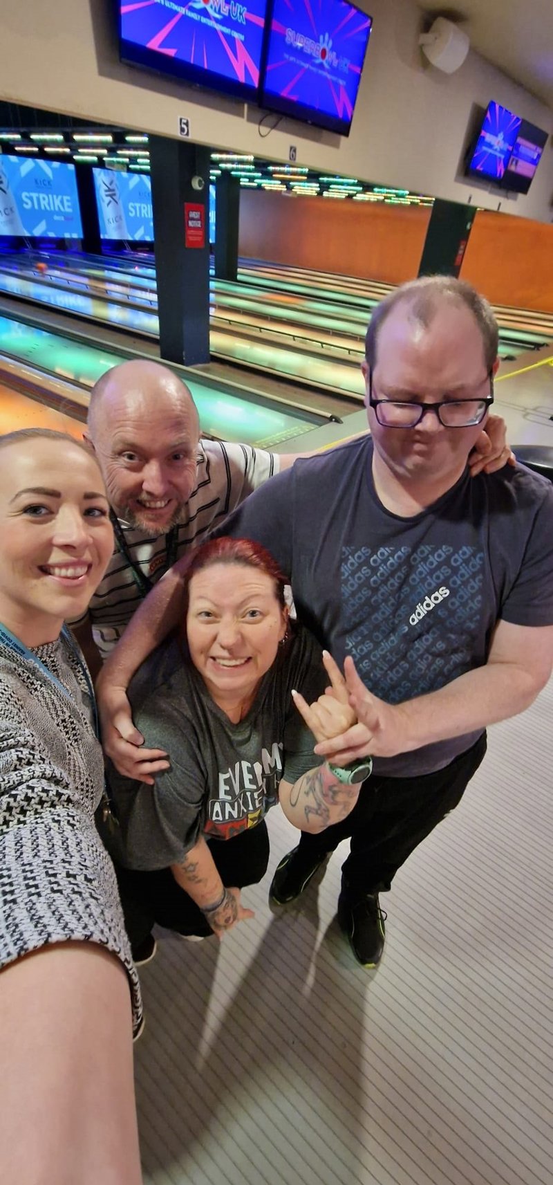 Four residents and staff smiling together at a bowling alley during an Oakhill group outing