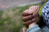 Adult's hand gently cradling a baby's bare foot outdoors at Victoria Villas family assessment centre