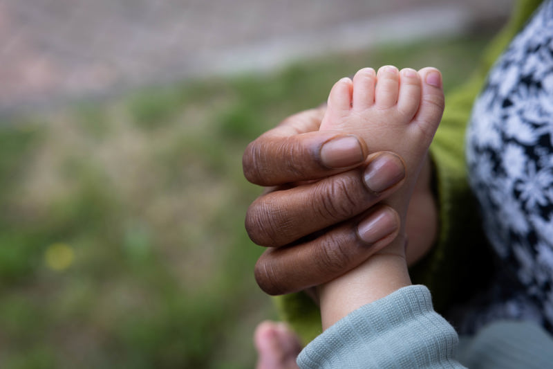 Adult's hand gently cradling a baby's bare foot outdoors at Victoria Villas family assessment centre