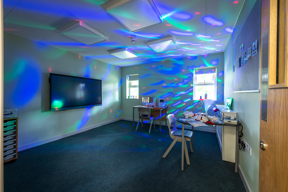 Dark sensory room with bright blue and green lights reflecting off the walls.