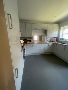 Kitchen at Rosewood with white gloss units, wooden worktops, a microwave and a grey floor