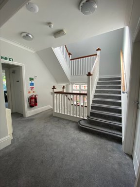 Carpeted staircase and upstairs landing at Eilat with white balustrade and fire exit signage