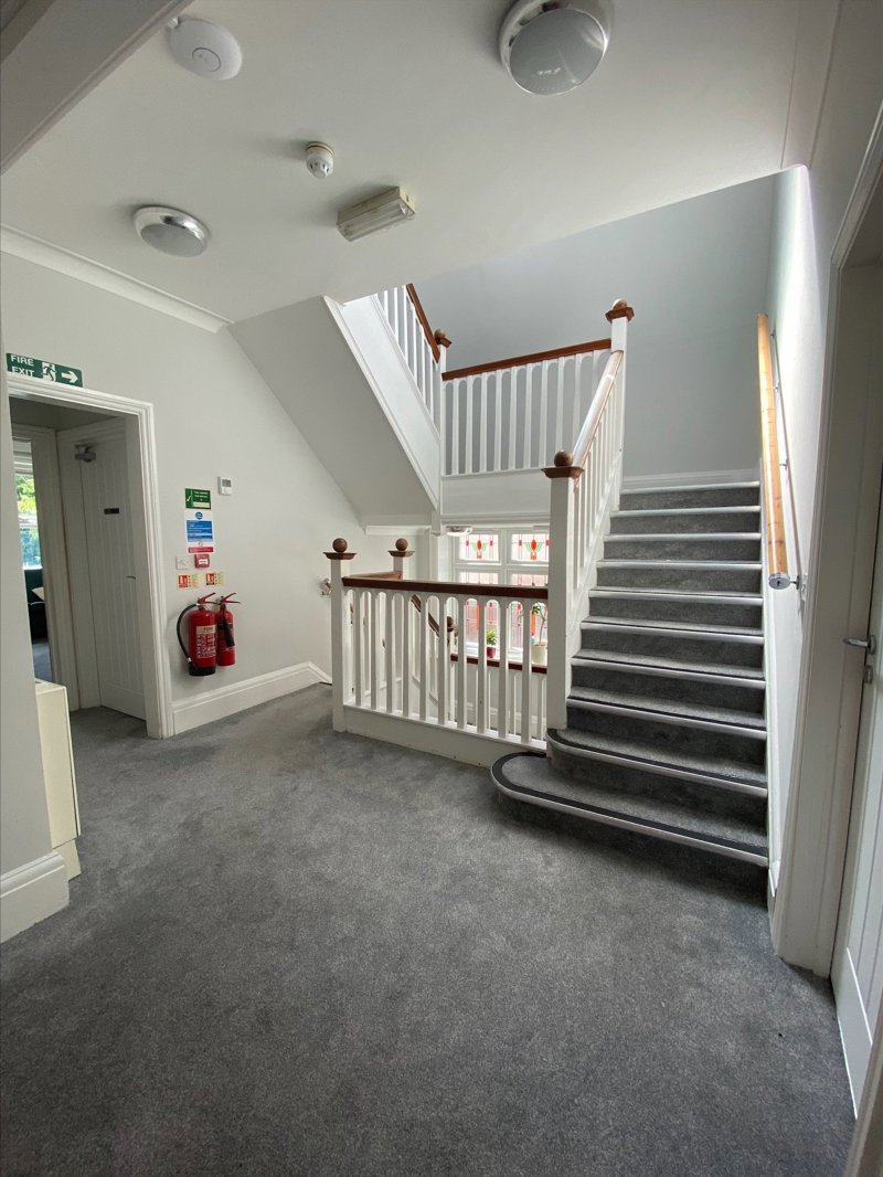 Carpeted staircase and upstairs landing at Eilat with white balustrade and fire exit signage