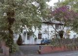 Exterior of The Grove, a white-rendered house behind mature trees with a low brick wall and a car parked outside