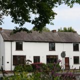 White-rendered cottage exterior of The Old Posting Office with dark window frames and a slate roof