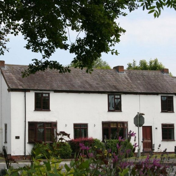 White-rendered cottage exterior of The Old Posting Office with dark window frames and a slate roof