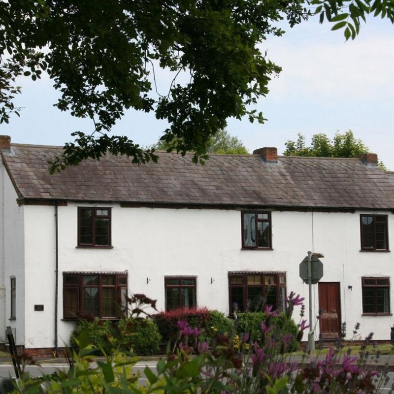 White-rendered cottage exterior of The Old Posting Office with dark window frames and a slate roof
