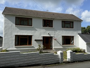 Exterior of Ty Arfryn, a white-rendered detached two-storey house with brown-framed windows, a tiled roof and a name plaque by the door