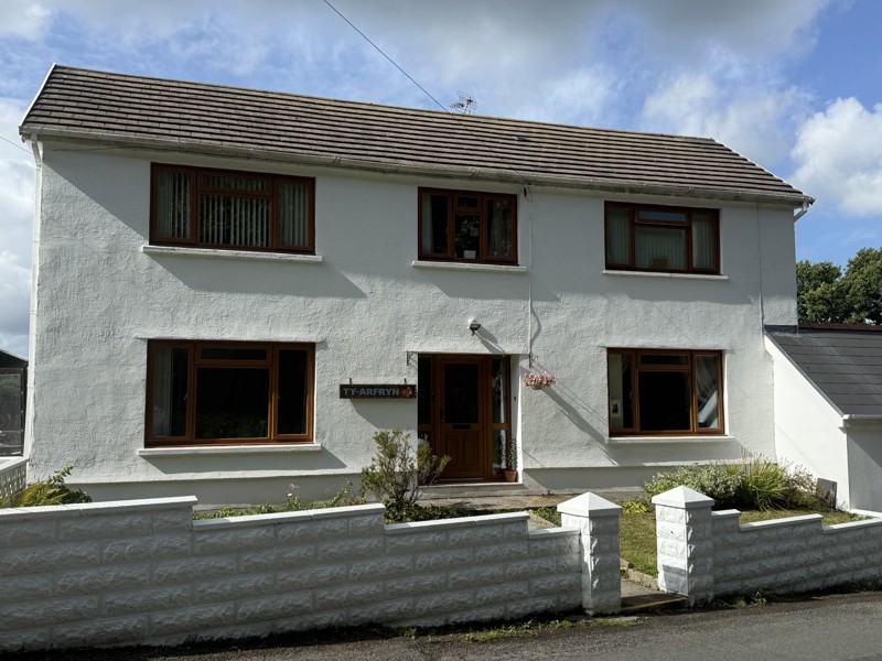 Exterior of Ty Arfryn, a white-rendered detached two-storey house with brown-framed windows, a tiled roof and a name plaque by the door