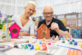 Two people painting wooden birdhouses at a craft table in a conservatory at Wyboston Lodge