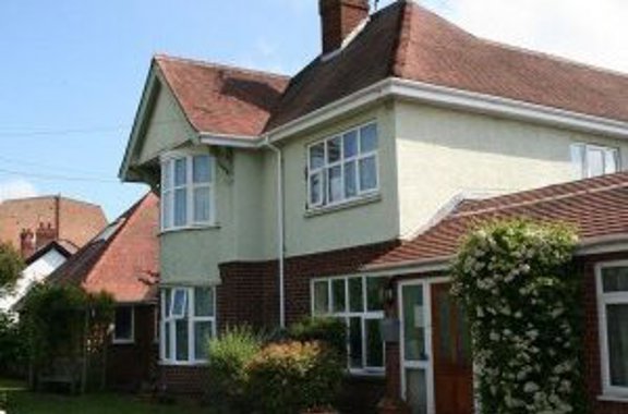 Exterior of Sunnydale, a rendered house with red-brick bay windows, a tiled roof and a small front lawn