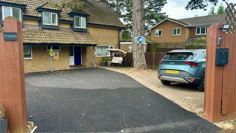 Driveway and front of Pinetrees seen from the gate, with the Pinetrees name sign and a parked car