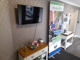 Reception lounge at Boston House with a wall-mounted TV, console table and an Accomplish information banner