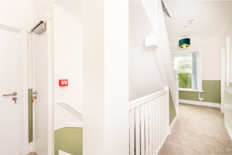 Upstairs landing at Brynawel with a white balustrade, sage green dado and a carpeted bedroom beyond