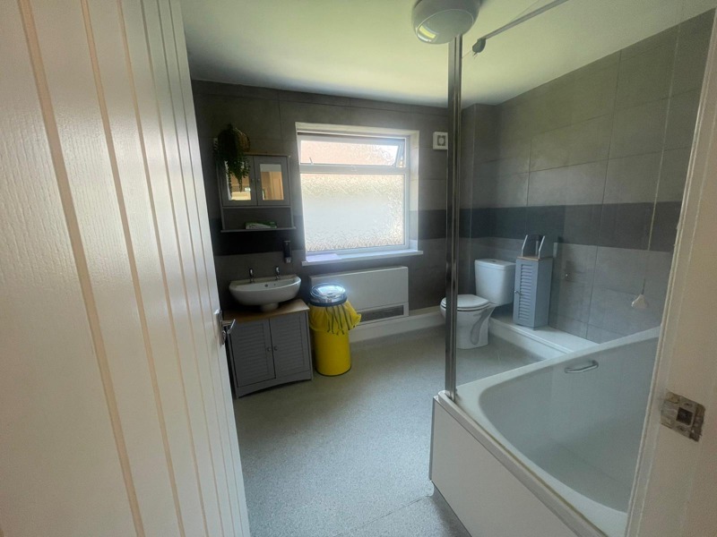 Bathroom at Rosewood with a white bath and shower screen, toilet, basin and grey tiled walls