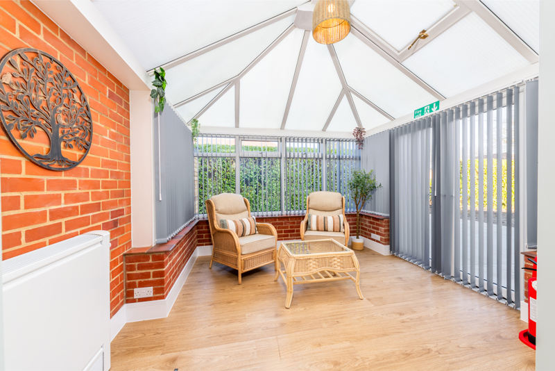 Conservatory at Church Road with rattan armchairs, a brick feature wall and garden views
