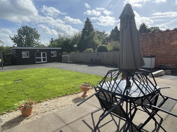 Patio and garden at Birchwood House with a glass table, parasol and lawn beyond