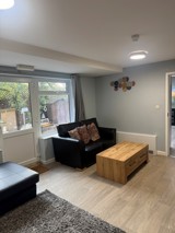 Lounge at Pinetrees with black leather sofas, a wooden coffee table and a window onto the garden