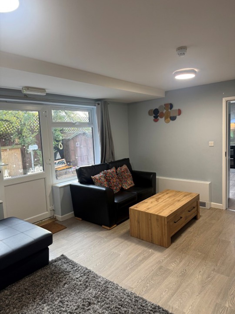 Lounge at Pinetrees with black leather sofas, a wooden coffee table and a window onto the garden