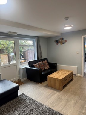 Lounge at Pinetrees with black leather sofas, a wooden coffee table and a window onto the garden