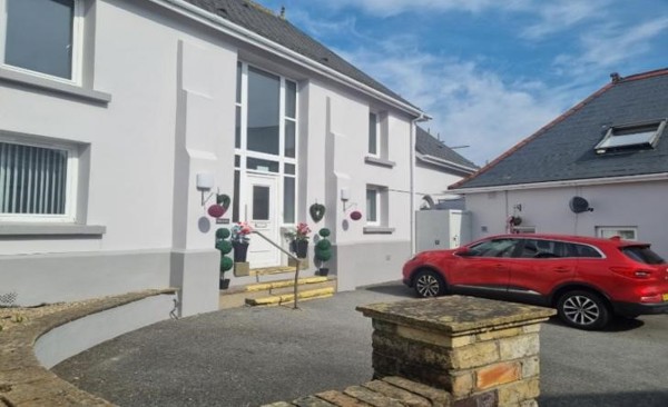 White-rendered exterior of Ty Llewellyn with a central front door, topiary plants and a red car on the driveway