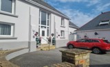 White-rendered exterior of Ty Llewellyn with a central front door, topiary plants and a red car on the driveway