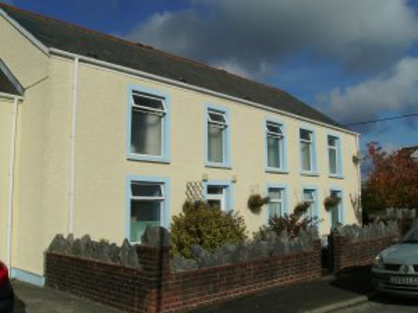 Front exterior of Rose Cottage, a cream-rendered two-storey house behind a low stone wall