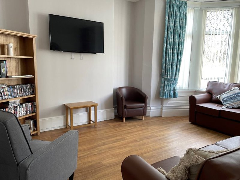 Front lounge at Princes Court with a wall-mounted TV, a DVD bookcase, leather and fabric seating and a bay window