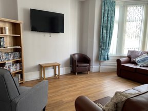 Front lounge at Princes Court with a wall-mounted TV, a DVD bookcase, leather and fabric seating and a bay window