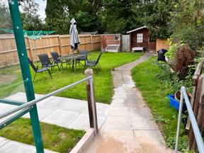 Back garden at Chesterwood with a paved path to a summer house, lawn and patio seating