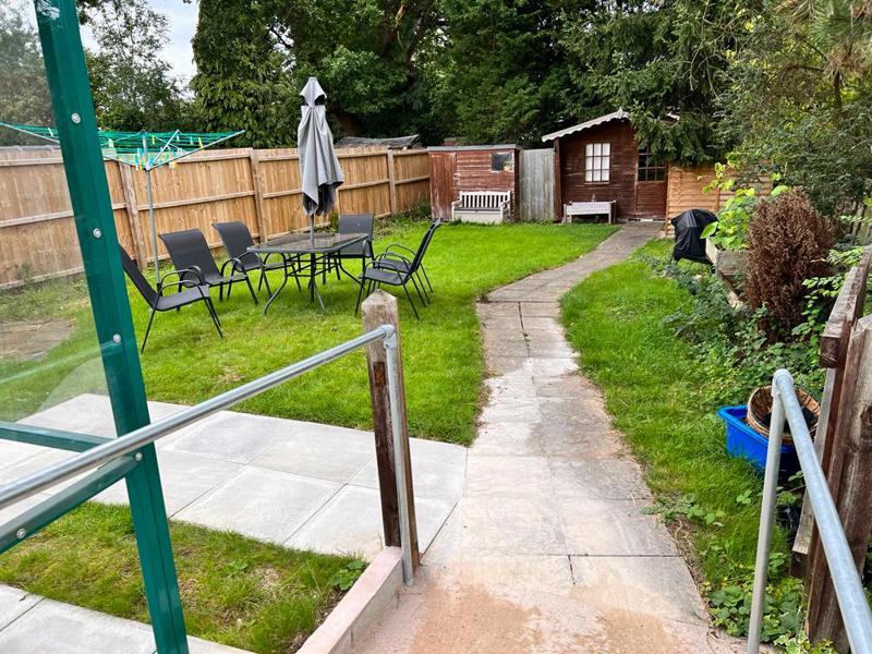 Back garden at Chesterwood with a paved path to a summer house, lawn and patio seating