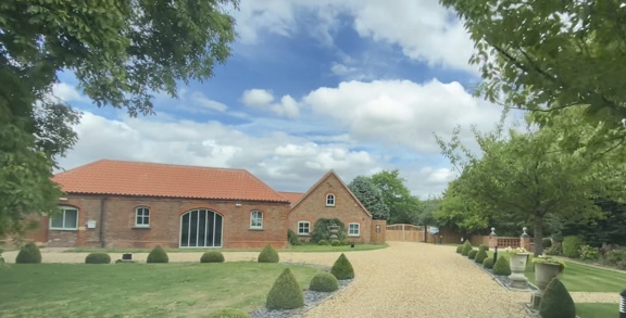 Front exterior of Heckington House, a red-brick building with an orange tiled roof, lawn, topiary and a gravel drive.
