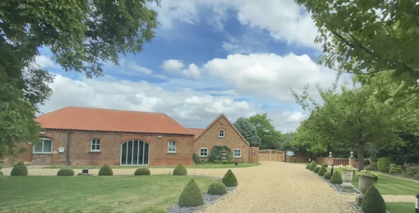 Front exterior of Heckington House, a red-brick building with an orange tiled roof, lawn, topiary and a gravel drive.
