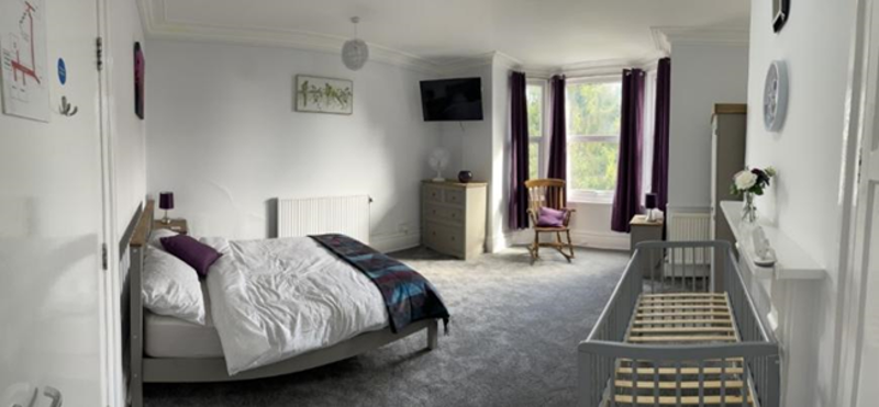 Spacious bedroom at Crown House with a double bed, baby cot and wooden rocking chair by a bay window