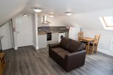 Open-plan loft living area at Willow Lodge with a brown sofa, dining table and a fitted kitchenette