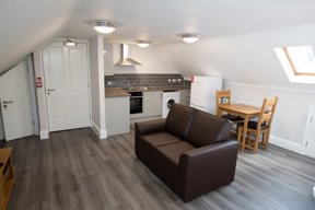 Open-plan loft living area at Willow Lodge with a brown sofa, dining table and a fitted kitchenette